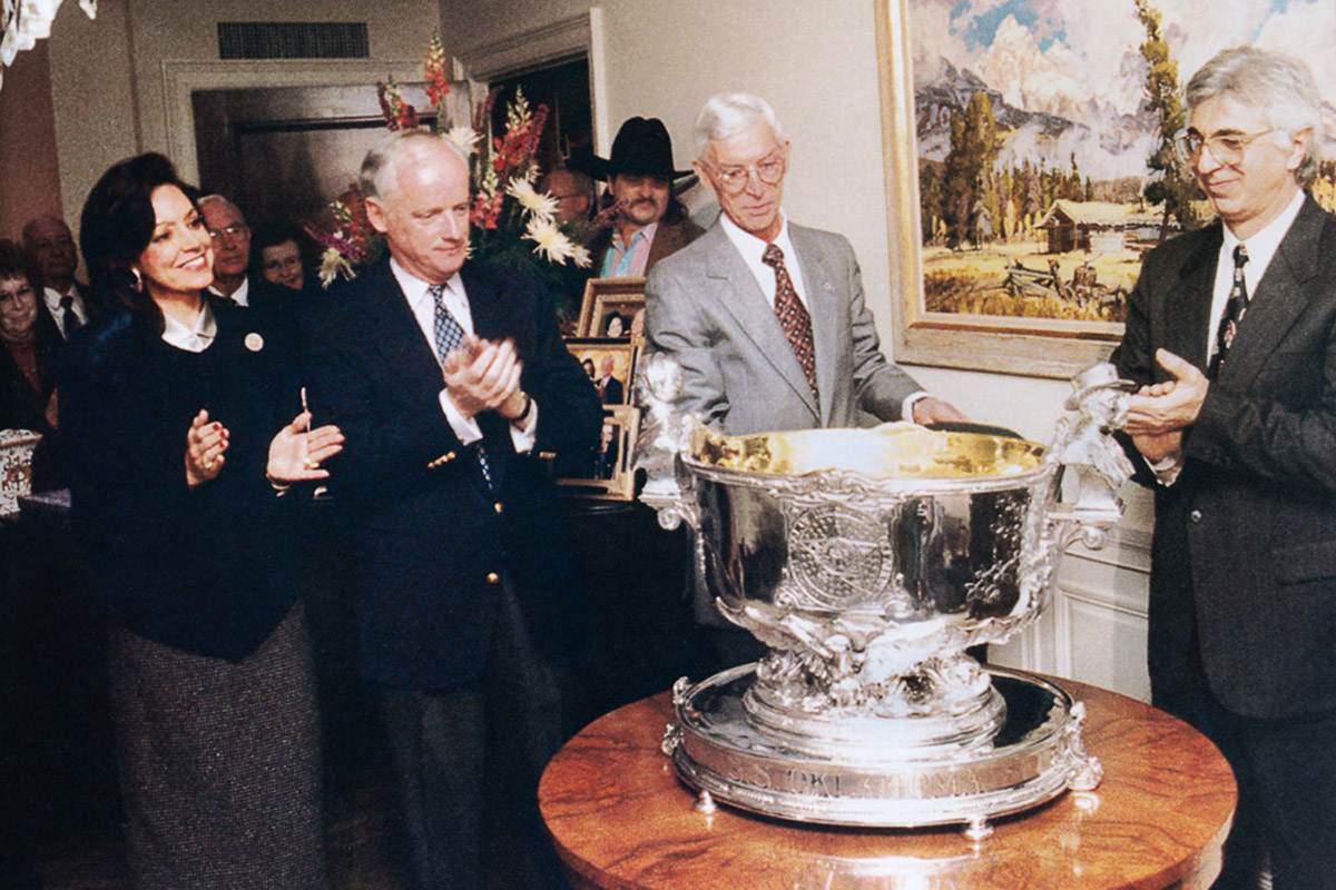 Silver sculpture artist Michael Galmer at the unveiling of the USS Oklahoma punch bowl at the Oklahoma Governor's Mansion, with Governor Frank Keating. Taken from the book titled 'The House Oklahoma Built: A History of the Oklahoma Governor's Mansion', 2001